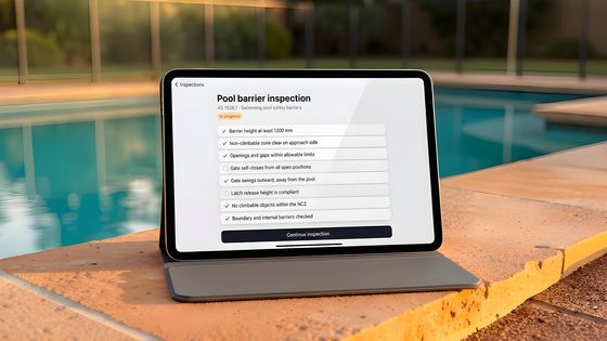 A pool barrier checklist on a tablet beside a pool